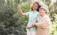 Elder woman and nurse strolling in the park